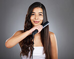 Portrait, woman and hair straightener for care, natural beauty or treatment on grey studio background. Female, girl and salon equipment for luxury, ironing hair style and grooming routine for styling