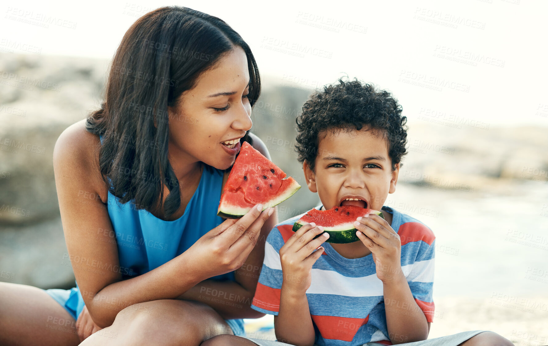 Buy stock photo Shot of a mother and sitting down and enjoying some watermelon at the beach