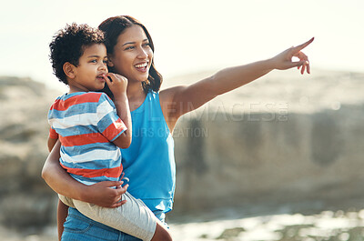 Buy stock photo Shot of a young mother holding her son at the beach pointing at the view