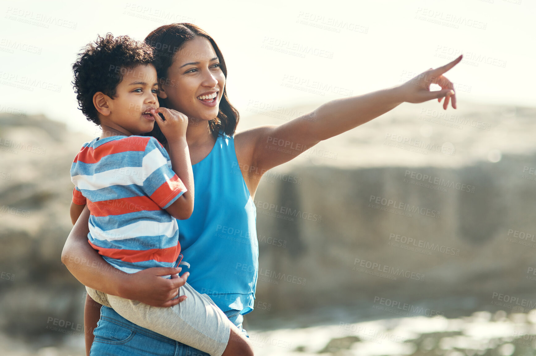 Buy stock photo Shot of a young mother holding her son at the beach pointing at the view