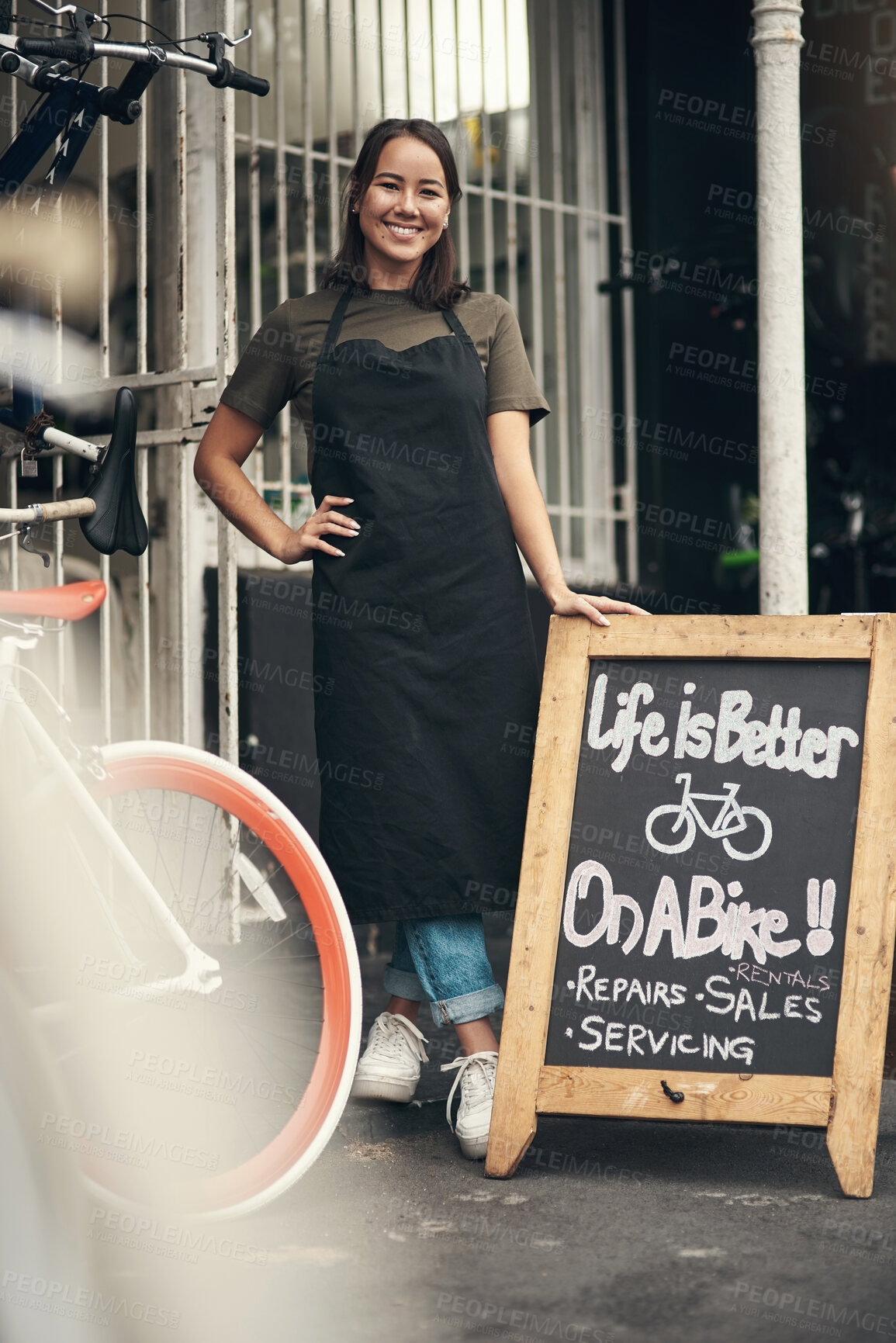 Buy stock photo Full length shot of an attractive young woman standing outside her bicycle shop during the day
