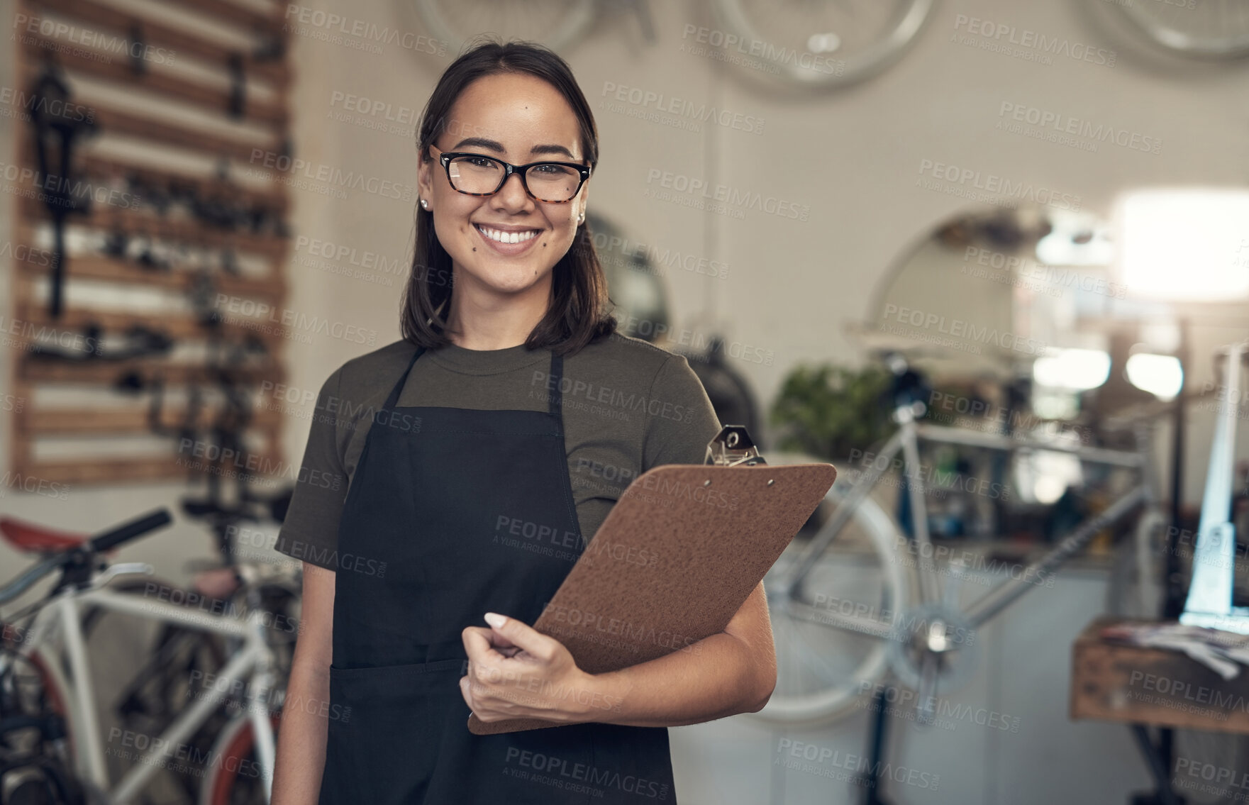 Buy stock photo Shot of an attractive young woman standing alone in her bicycle shop and holding a clipboard