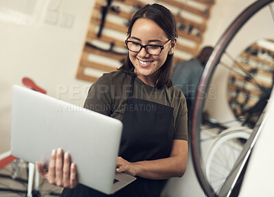 Buy stock photo Shot of an attractive young woman standing alone in her bicycle shop and using her laptop