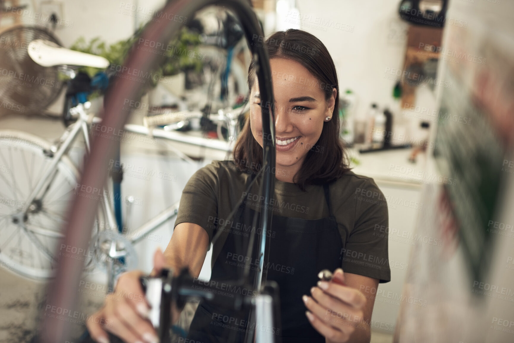 Buy stock photo Shot of an attractive young woman standing alone in her shop and repairing a bicycle wheel