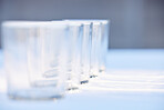 Glass, crockery and mockup with a row of drinking glasses on a table in a studio or restaurant for fine dining. Space, glassware and drinks with a group of cups in a line for a beverage while dining