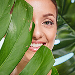 Portrait, skincare and palm leaf with a model woman posing in studio on blue background for beauty. Face, skin or nature with an attractive young female standing behind a plant for natural treatment