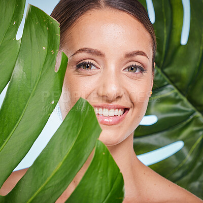 Buy stock photo Portrait, skincare and palm leaf with a model woman posing in studio on blue background for beauty. Face, skin or nature with an attractive young female standing behind a plant for natural treatment