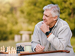 Senior man, park and thinking for chess, game and competition at table by trees, sunshine and focus. Elderly chess player, outdoor and strategy for contest in nature, relax and play in Los Angeles