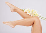 Legs, beauty and skincare with flower and natural glow with nature aesthetic, cosmetics and healthy skin against studio background. Feet, cosmetic care and shine with pedicure, wellness and orchid.