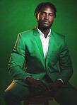 Fashion, formal and portrait of a black man in a suit sitting on a chair in studio with a luxury outfit. Elegant, stylish and African male model with fashionable clothes isolated by green background.