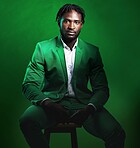 Fashion, formal and portrait of a black man in a suit sitting on a chair in studio with a luxury outfit. Elegant, stylish and African male model with fashionable clothes isolated by green background.