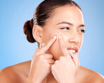 Skincare, beauty and woman squeeze pimple before a natural cosmetic face treatment in a studio. Acne, cosmetics and female model pop blackheads or facial scar with her fingers by a blue background.