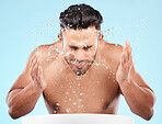 Face, water splash and skincare of man cleaning in studio isolated on a blue background. Hygiene, water drops and male model washing, bathing or grooming for healthy skin, facial wellness or beauty.