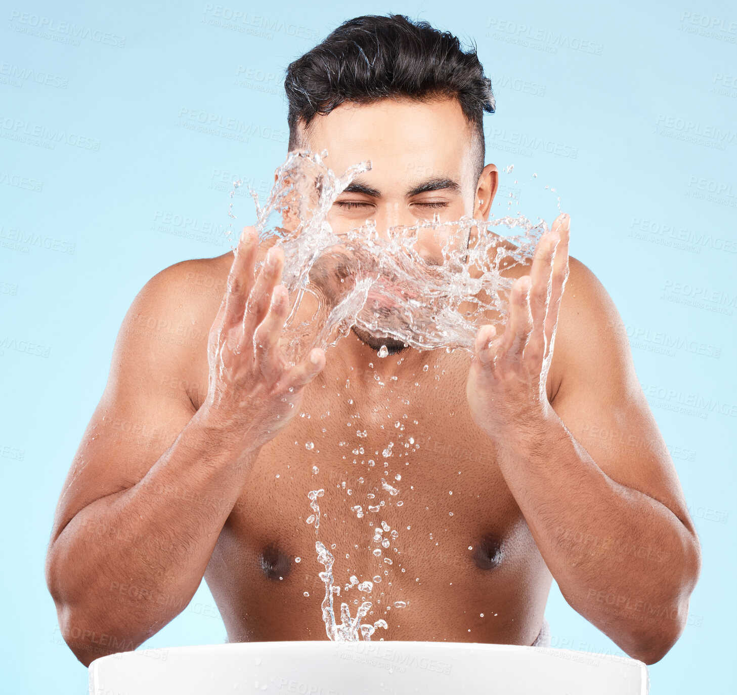Buy stock photo Face, water splash and skincare of man cleaning in studio isolated on a blue background. Hygiene, water drops and male model washing, bathing or grooming for healthy skin, facial wellness or beauty.