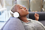 Headphones, sofa and black woman listening to music, radio or podcast while relaxing in her living room. Rest, calm and African girl streaming a song, album or playlist online while sleeping at home.