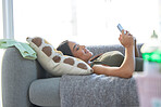 Indian woman, phone and relax happy on sofa for social media, online communication and streaming video on web mobile app. Female, calm peace and relaxation or happiness watching meme on smartphone 