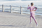 Woman, fitness and running by sea, outdoor and fast for wellness, health and goals in summer. Runner girl, speed and balance in sunshine with smartphone, wearable tech and waves by ocean in Cape Town