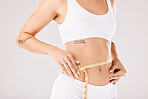 Fitness, weightloss and slim woman in a studio with a measuring tape on her body for motivation. Diet, health and girl model with a healthy, wellness and exercise routine isolated by gray background.