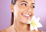 Beauty, wellness and woman with a lily flower in studio for a health, cosmetic and natural face routine. Skincare, health and healthy girl model from Brazil with floral isolated by purple background.