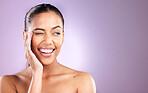 Woman, smile and wink for funny skincare wellness or face dermatology beauty in purple studio background. Model, facial cosmetics care and natural glowing skin or comic happiness or headshot vision