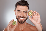 Man, face and beauty with kiwi, facial care with wellness and organic treatment against studio background. Natural skincare, exotic fruit and wellness with cosmetic care and smile in portrait