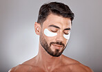 Skincare, beauty and man with mask for eyes on gray background for wellness, facial treatment and dermatology. Grooming, luxury spa and male with face patch, eye pads and cosmetics products in studio
