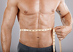 Man, body and tape measure on abdomen in studio on gray background. Health, fitness and male model with measuring tape for abs to track exercise training results, muscle goals or weight loss target.
