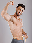 Portrait, body and weightloss with a man measuring his waist in studio on a gray background for diet progress. Fitness, heath and wellness with a topless male model flexing his strong bicep muscle
