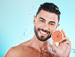 Skincare, water splash and portrait of man with grapefruit on blue background for vitamin c detox for healthy skin and smile. Fruit, water and facial wellness, spa cleaning and happy male model face.