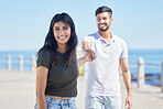 Beach, love and portrait of a happy couple holding hands while on a seaside summer vacation. Happiness, smile and young man and woman from India walking on the promenade by the ocean while on holiday
