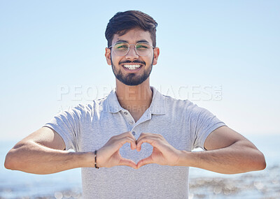 Buy stock photo Beach portrait and a man heart hand for summer holiday freedom, happiness and wellness. Happy Indian person enjoying ocean sun with love shape and optimistic smile for travel adventure.

