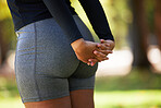 Stretching, hands and butt of woman at park for health, wellness and flexibility. Sports, training and female athlete outdoors in nature preparing, warm up and getting ready for workout or exercise.