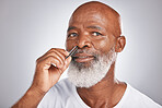 Senior man, nose hair and tweezer for self care, hair removal and epilation for beauty and grooming . Headshot of black male with beard on grey studio background for body care, hygiene and clean skin