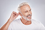Elderly man, ear cleaning with cotton swab for hygiene, grooming and clean body with cosmetic care against studio background. Beauty, health and wellness, senior male and happy with natural cosmetics