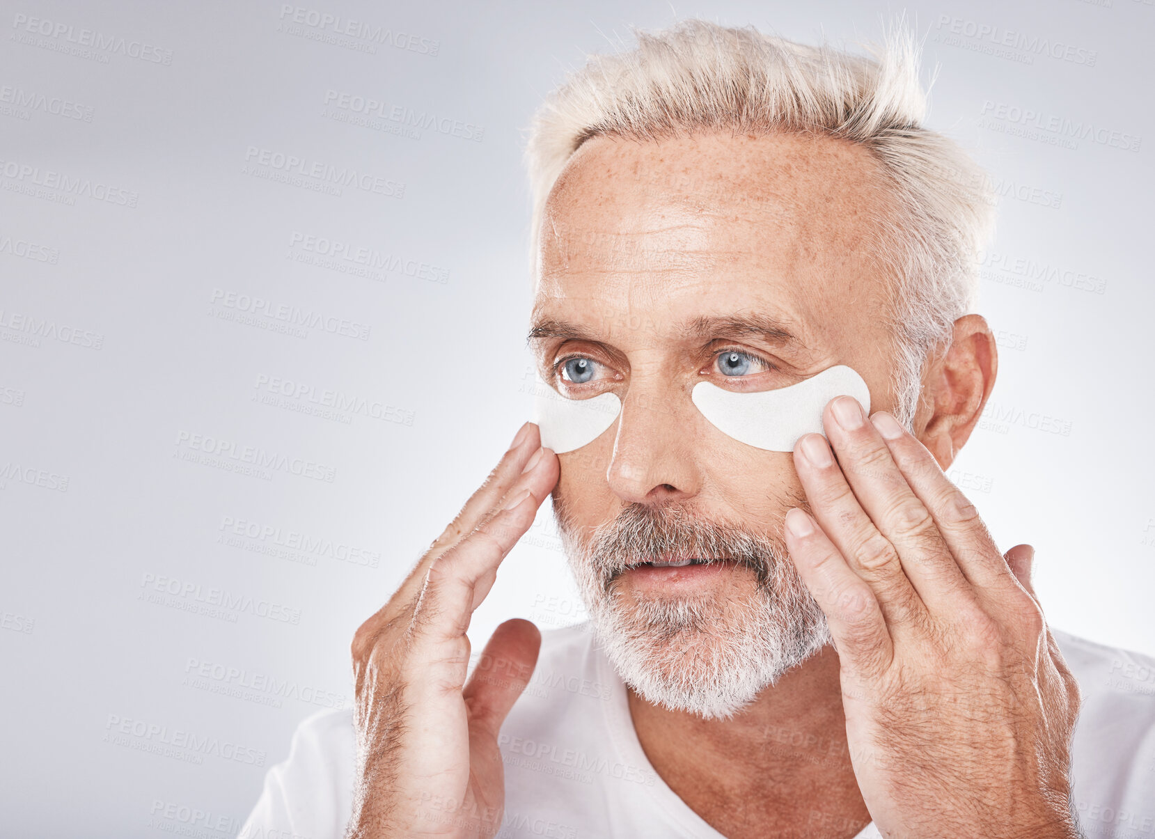 Buy stock photo Skincare, eyes patch and man in studio for dermatology facial, face cosmetics or collagen mask advertising or marketing mockup. Senior model, hands application and eye patches or anti aging product
