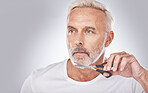 Facial hair, cutting and man with scissors for grooming, shaping and routine treatment on a studio background. Barber, cleaning and face of a senior model trimming beard during morning clean