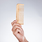 Hand, comb and haircare with a man barber in studio on a gray background for grooming or hair styling. Salon, bamboo and beauty with a male hairdresser holding a tool to groom or style closeup indoor
