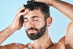 Face, hair care shower and water splash of man in studio isolated on a blue background. Dermatology, water drops and male model washing, cleaning and bathing for healthy skin, skincare and hygiene.
