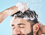 Face, water splash and man in shower with shampoo in studio on a blue background. Skincare dermatology, water drops and male model cleaning, bathing or washing for hair care, hygiene and wellness.