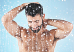 Face, water splash and skincare shower of man in studio isolated on a blue background. Dermatology, water drops and male model bathing, washing or cleaning for hygiene, wellness and healthy skin.