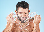 Man, splash and face for beauty in studio for wellness, health or self care cleaning by blue background. Model, bathroom and water drops with hands for healthy facial, self love and cosmetic backdrop