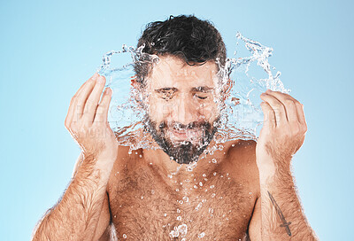 Buy stock photo Face, splash and man in studio for cleaning, wellness and personal health with self care by blue background. Model, facial and healthy with water splash, skincare and cosmetics by studio backdrop