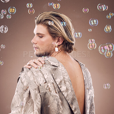 Buy stock photo Beauty, lgbtq fashion and man with bubbles in studio on brown background for cosmetics, style and modern outfit. Creative art, luxury design and non binary model with soap bubbles, jewelry and makeup