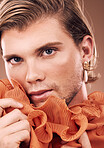 Lgbtq, fashion and portrait of man with makeup, beauty and creative orange clothes on studio background. Transgender, face and queer model with skincare cosmetics, gay pride and non binary identity