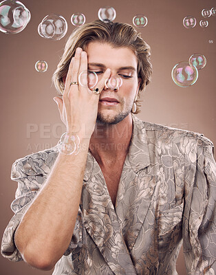 Buy stock photo Beauty, fashion and man with bubbles in studio on brown background for cosmetics, style and modern outfit. Creative art, luxury design and male fashion model with soap bubbles, jewellery and makeup