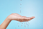 Hand, water and hydration with a woman cleaning in studio on a blue background for hygiene or personal care. Water splash, health and skincare with a female washing hands in the shower or bathroom