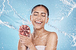 Skincare, water splash and woman with a pomegranate in a studio for a healthy, organic and natural face treatment. Wellness, health and girl model with a fruit for a facial routine by blue background