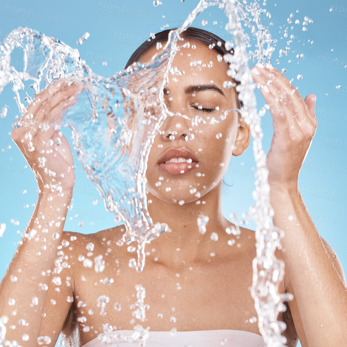 Buy stock photo Woman, hands or washing face in water splash on blue background studio for dermatology healthcare, hygiene wellness or self care grooming. Beauty model, facial cleaning or wet water drops in bathroom