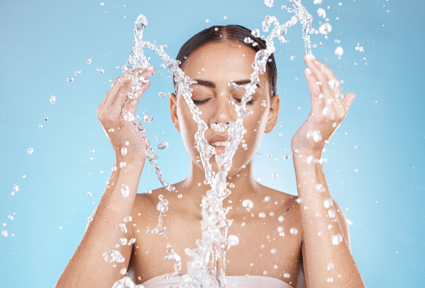 Buy stock photo Woman, skincare or washing face with water splash on blue background studio for healthcare wellness, hygiene maintenance or bathroom grooming. Beauty model, hands or facial cleaning with water drops