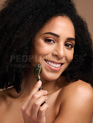 Buy stock photo Face portrait, skincare and black woman with roller in studio on a brown background. Makeup, cosmetics and happy female model holding jade stone product for facial massage, healthy skin and beauty.